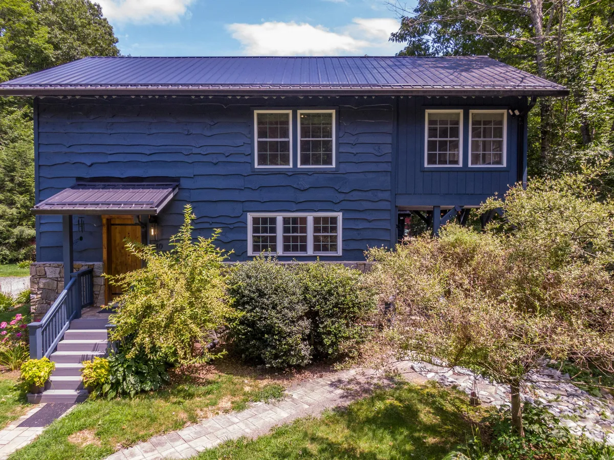 A welcoming exterior scene showing the blue wooden siding of the house, landscaped garden, stone pathway, and large windows. The space is open and inviting, ideal for outdoor games and activities that families can enjoy together.