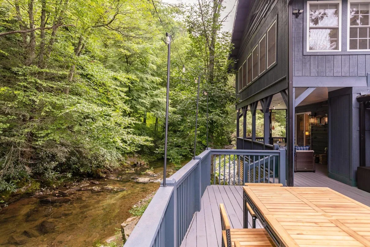 An exterior deck overlooking the creek, featuring a wooden dining table surrounded by greenery. The space is ideal for outdoor dining, morning coffee, or grilling while enjoying the river’s soothing sounds.