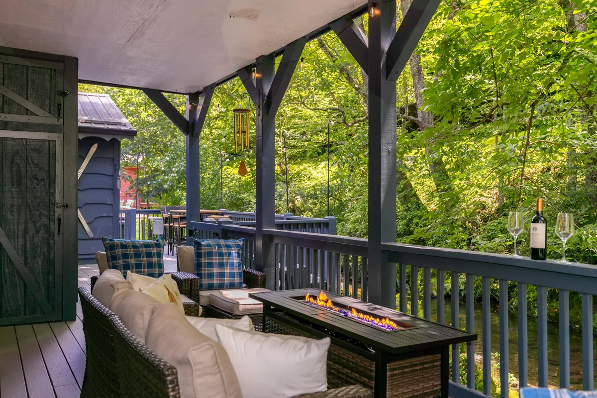 A cozy riverside fire pit surrounded by comfortable outdoor seating, all nestled in lush greenery. Wine glasses on the table hint at gatherings, and the placement suggests a perfect spot for evening campfires, marshmallow roasts, and sharing stories under the stars.