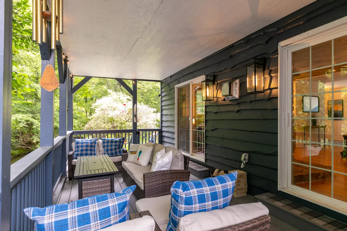 A welcoming outdoor seating area with plaid cushions and lantern-style lighting sits under a canopy of trees. The inviting setup suggests a comfortable place for guests (and their dogs) to relax after exploring Boone’s trails.
