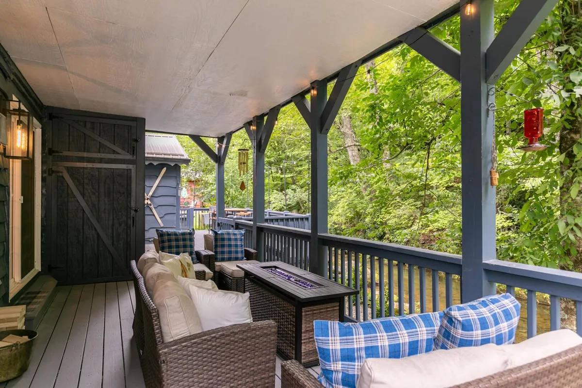 A cozy outdoor seating area framed by a wooden railing, surrounded by lush greenery. Comfortable chairs invite guests to relax and soak in the peaceful natural setting, with hints of morning or evening light filtering through the trees.