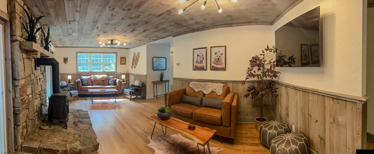 A warm, inviting living area featuring a prominent stone fireplace, a plush brown leather sofa, a wooden dining table, and wall art. The crackling fire and cozy furniture create the ideal space to relax after a day in the mountains, while the open layout makes it perfect for gathering and unwinding.