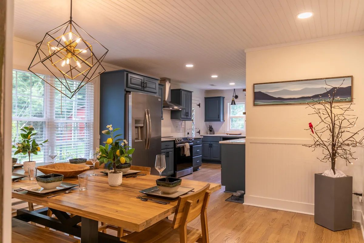 A warm, inviting dining area featuring a large dining table, a kitchen island, pendant light fixtures, and decorative touches like a tree branch centerpiece. The layout encourages family meals, group celebrations, and shared moments.
