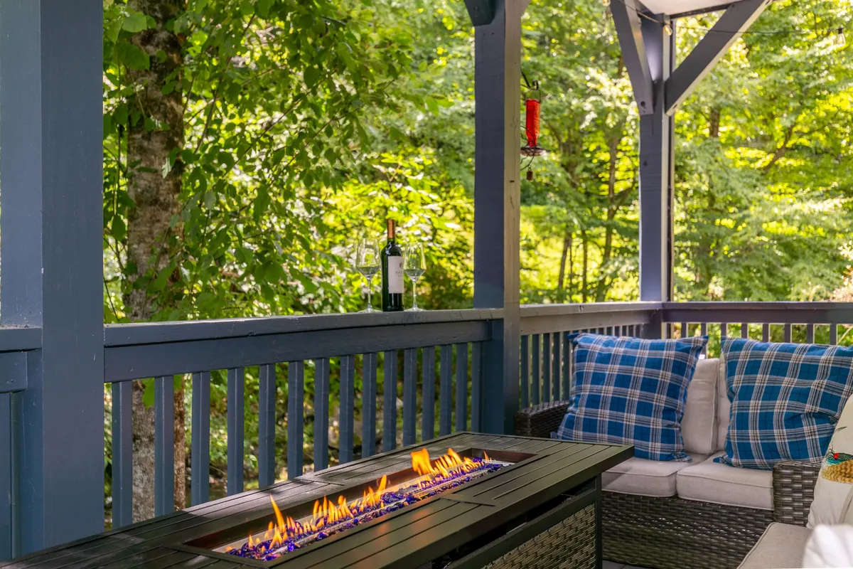A cozy fire pit area with cushioned seating, bottles of wine, and surrounding greenery. The arrangement is perfect for socializing, sharing stories, and relaxing under the stars with friends or family.