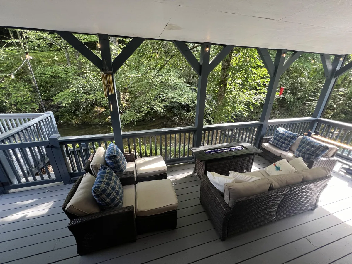 A serene exterior space featuring comfortable seating overlooking a flowing creek and dense greenery. The scene evokes relaxation, with the gentle sound of water adding to the atmosphere of seclusion and serenity.