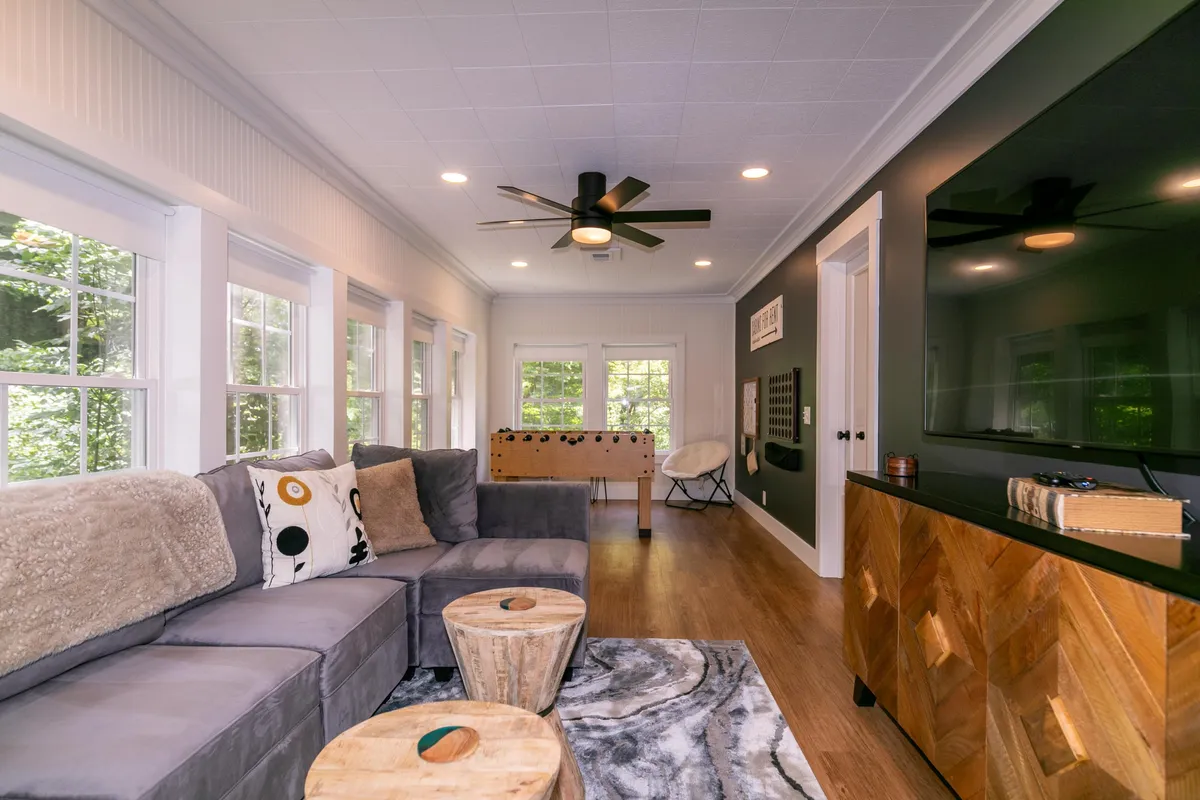 A casual and welcoming scene with a plush sofa, game table set up for board games, a TV, and wooden stools. The layout encourages both relaxation and active engagement, with options for movie nights, friendly competition, and group conversations all within the same open area.